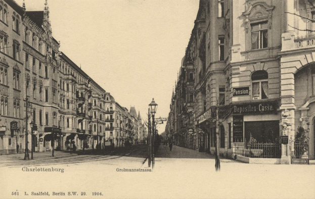 Schwarz-weiß-Fotografie einer Straße in Charlottenburg, Deutschland, mit Gebäuden, Straßeninfrastruktur, Kraftfahrzeugen, Füßgängern und einem klaren Himmel.