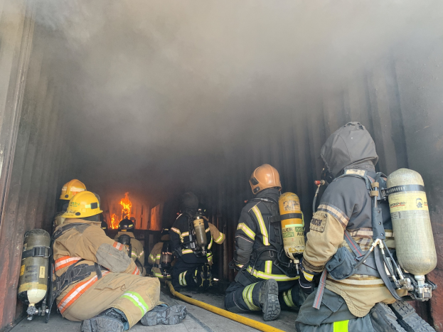 Feuerwehrleute in Helmen und Sauerstoffflaschen sitzen im Rückteil eines rauchgefüllten Lkws bei einer Öbung an der University of California, Berkeley, mit einem große Feuer im Hintergrund.