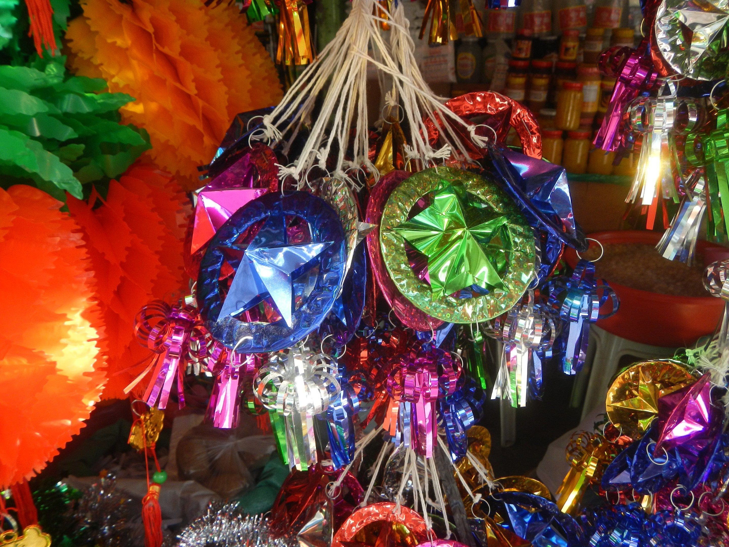 Farbenfrohe Dekorationen wie Laternen, Bänder und andere Gegenstände hängen von der Decke über Regalen mit Flaschen in einer festlichen Atmosphäre.