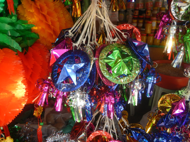 Farbenfrohe Dekorationen wie Laternen, Bänder und andere Gegenstände hängen von der Decke über Regalen mit Flaschen in einer festlichen Atmosphäre.