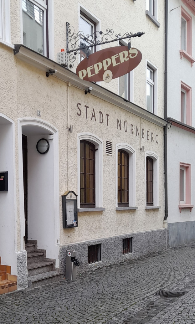 Außenansicht eines Gebäudes mit einem "Stadt Nurnberg"-Schild, Fenstern, einer Tür, einer Treppe und einem Müllcontainer im Vordergrund.
