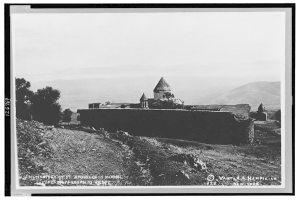 Ein Schwarz-Weiß-Foto eines Klosters, umgeben von Bäumen, Hügeln und einem klaren Himmel, mit Text unten.