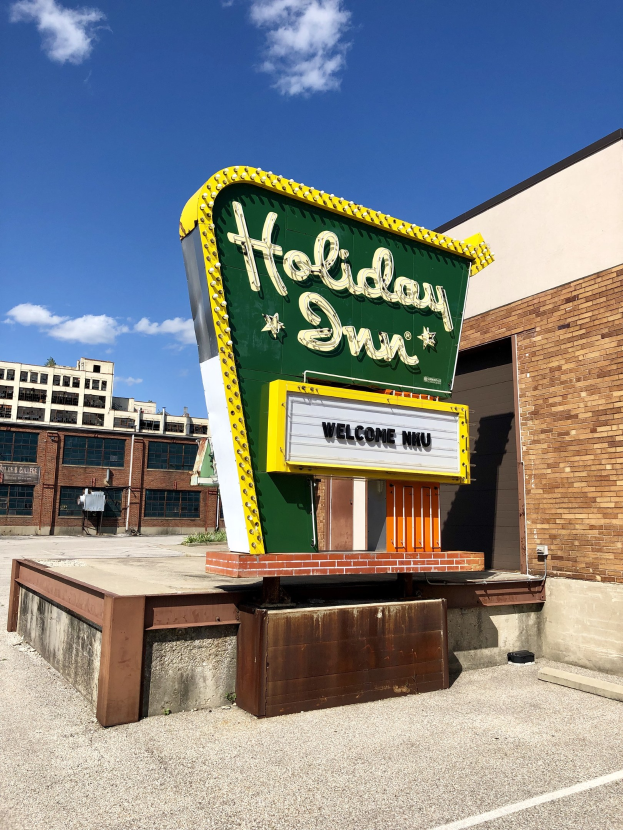 Holiday Inn Schilder an einem Gebäude mit einer Texttafel davor, bewölktem Himmel und sichtbaren Fenstern auf dem Gebäude.