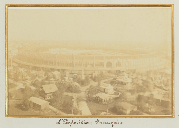 Altes Schwarz-Weiß-Foto eines Stadions umgeben von Stadtgebäuden, Bäumen und Strommasten mit Text unten.