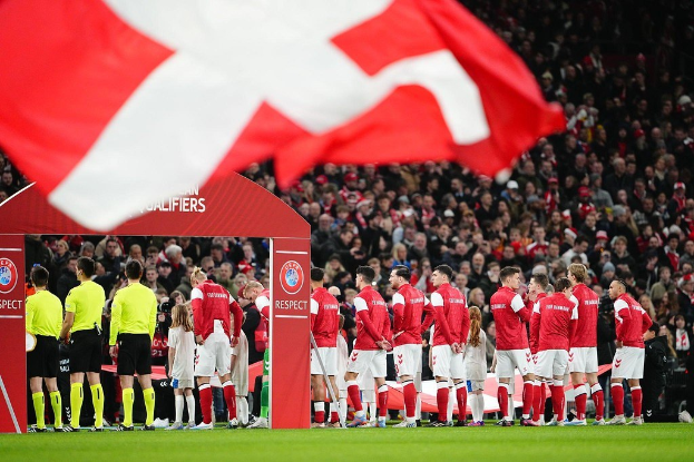 Eine Gruppe von Menschen auf einem Fußballfeld mit einer roten und weißen Flagge im Vordergrund, einem Bogen mit der Aufschrift "Bayern München vs Bayern München Betting Tips & Preview" im Hintergrund und einer großen Menge im Stadion.