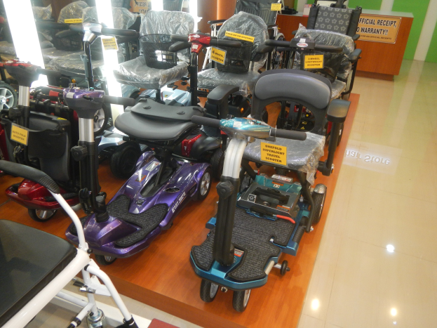 Reihe von E-Scootern im Geschäft mit Preisschildern, einem Holztisch mit einer Tafel im Hintergrund und sichtbarem Boden.