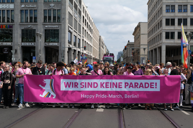 Eine Gruppe von Menschen geht auf der Straße in Berlin, Deutschland, mit einem pinken Banner mit der Aufschrift "Happy Pride March"