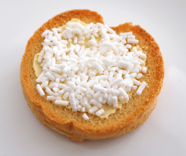 Ein herzförmiges Brotstück auf einer weißen Oberfläche, mit Butter und Zucker beträufelt.