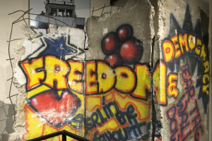 Wand mit Graffiti in dicken schwarzen Buchstaben "Freiheit und Demokratie", ein Gelönder unten und ein Fenster im Hintergrund.