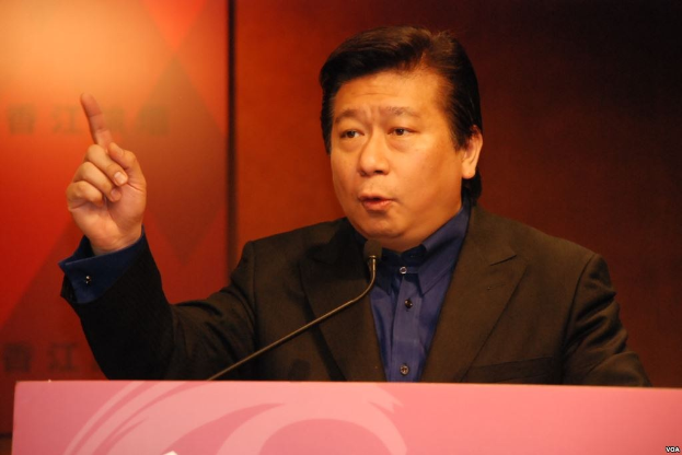 Ein Mann in Anzug und Krawatte, der eine Rede an einem Rednerpult mit Mikrofon hält und ernst wirkt.