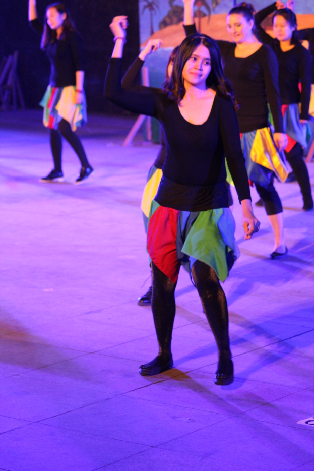 Gruppe junger Frauen auf der Bühne tanzend, mit Schuhen während einer Vorstellung, mit einem Gemälde im Hintergrund sichtbar.