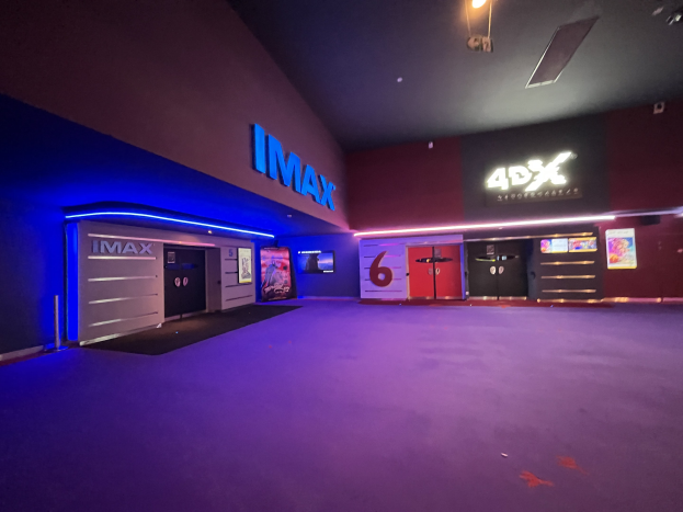 Innenseite eines Kinos mit lila Teppich, Text und Bildschirmen an den Wänden und Deckenbeleuchtung.