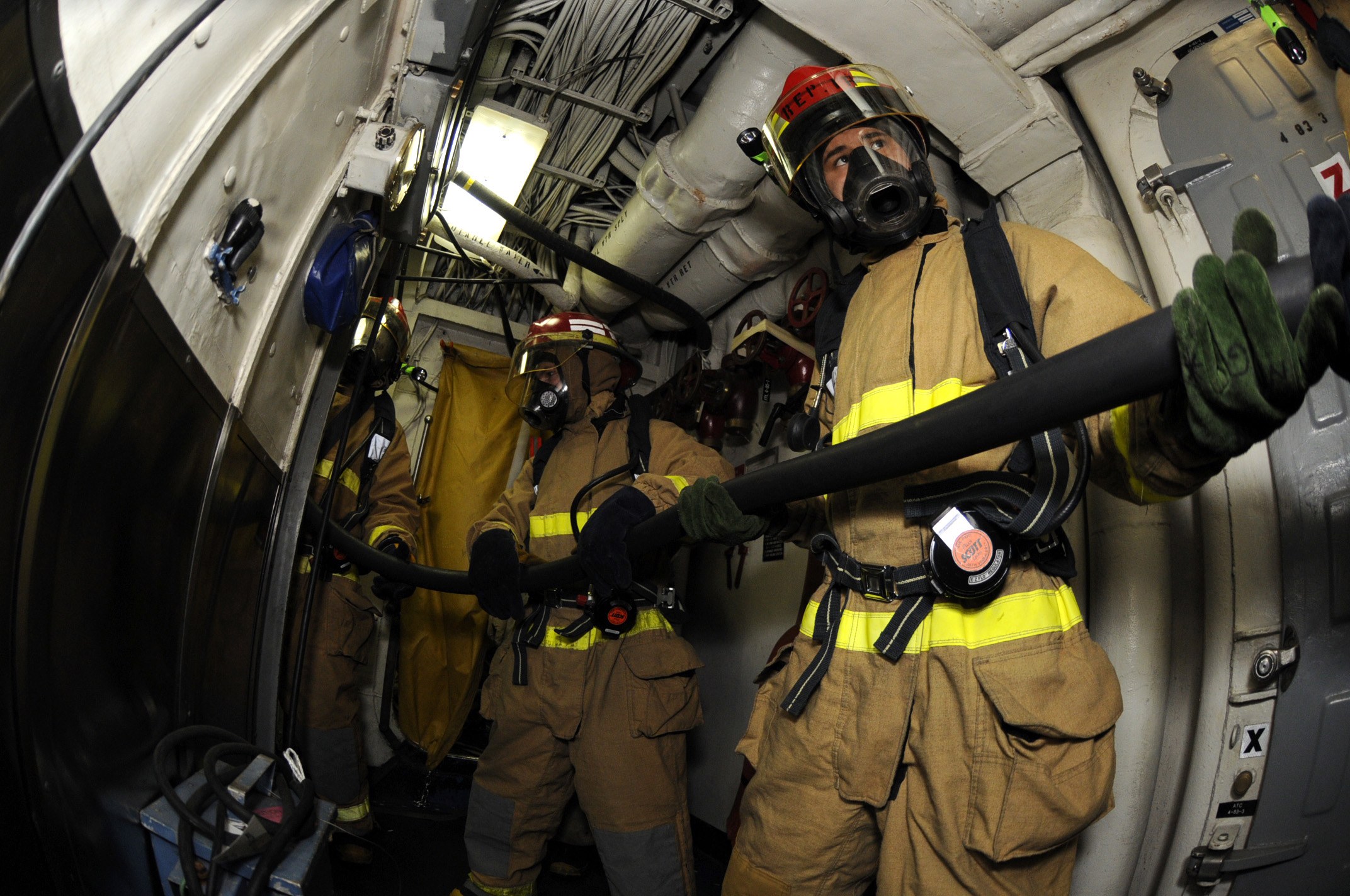 Feuerwehrleute in Helmen und Handschuhen mit einer Schlauchleitung in einem Flugzeug mit Ausrüstung und Text im Hintergrund.