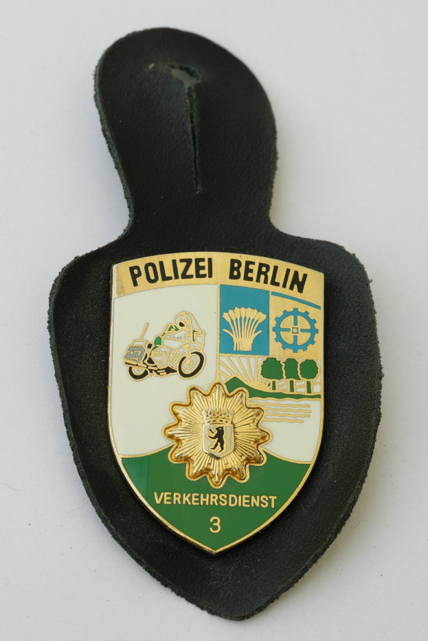 Ein schildförmiges Polizeibadge mit der Aufschrift "Polizei Berlin" auf einem blauen Hintergrund, einem weißen Stern und einem weißen Rand, das auf einer Oberfläche liegt.
