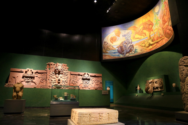 Ein Museumsraum mit verschiedenen Artefakten, darunter Skulpturen, Tischgegenstände, eine Texttafel, eine Wandmalerei und Deckenleuchten im Mexiko-Stadt-Museum für Anthropologie.