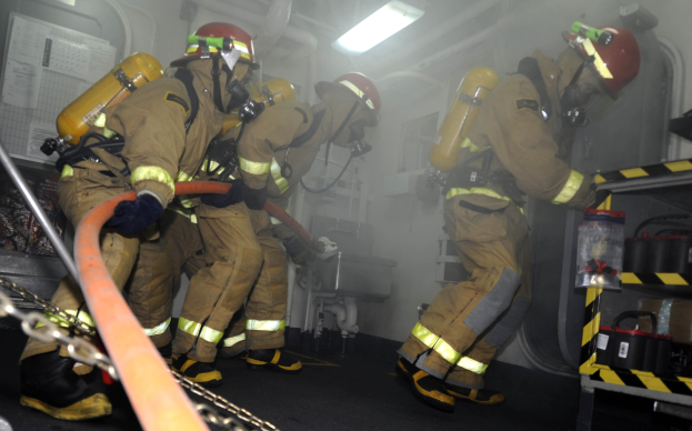 Feuerwehrleute in Schutzausrüstung arbeiten an einem Löschfahrzeug mit Ausrüstungsgestellen und sichtbarem Hintergrund.