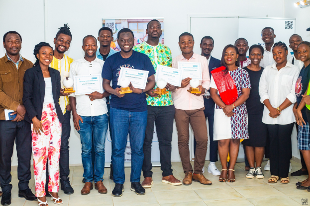 Eine Gruppe strahlender Menschen mit Urkunden, die neben einem Tisch mit Gegenständen und einem Plakat an der Wand stehen und die Gewinner der 2019 WIK Awards feiern.