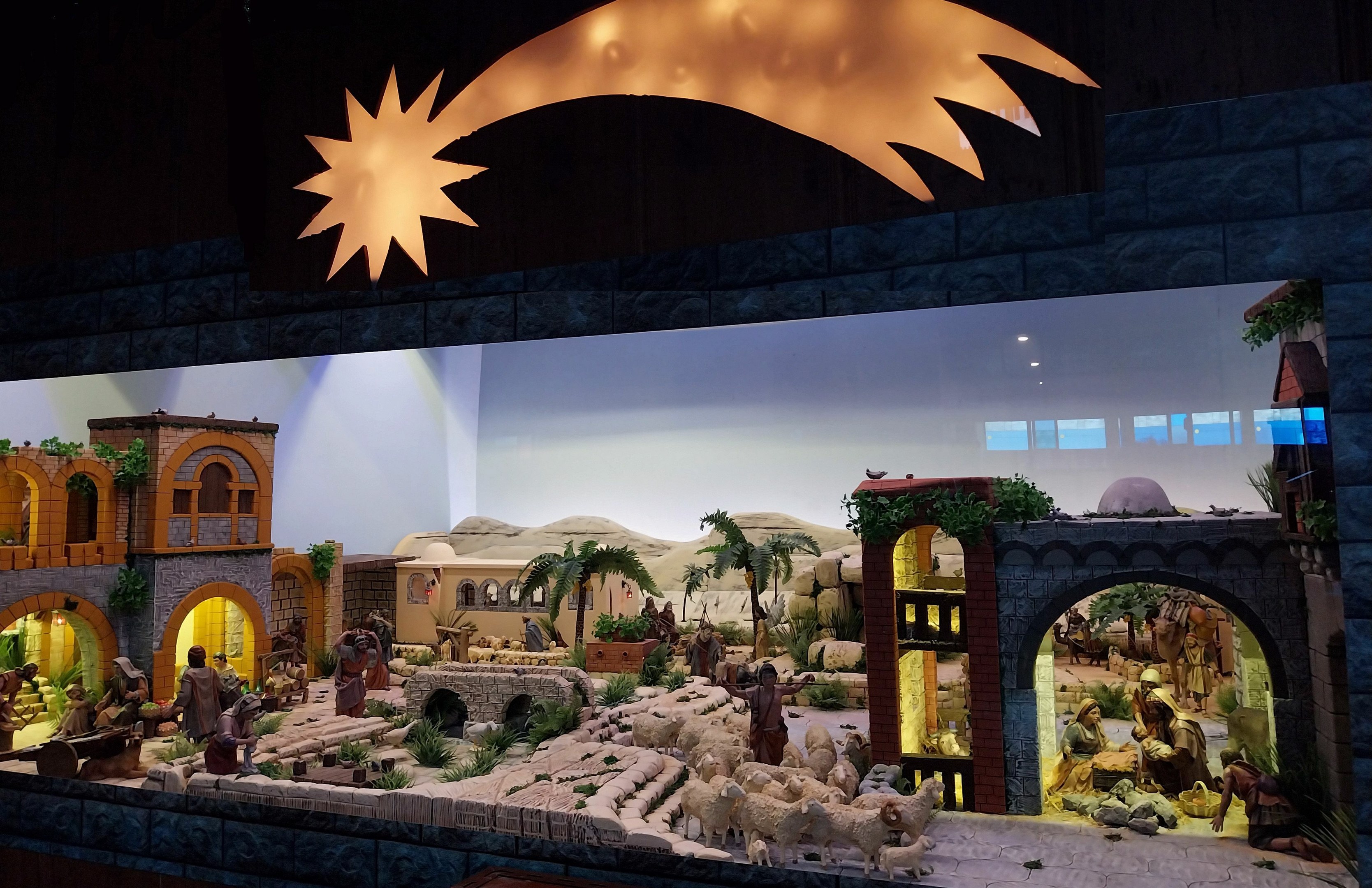 Eine Krippenausstellung im Museum mit Figuren, Tieren, Gebäuden und Grünpflanzen, beleuchtet von oben.