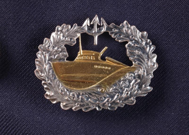 Ein goldener und silberner Abzeichen mit einem Boot, das die deutsche Marine darstellt, auf einem Tuch.