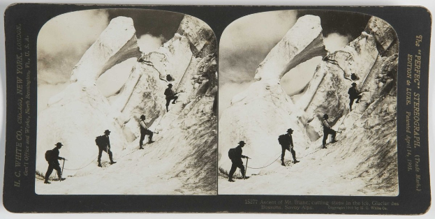 Schwarz-weißes Foto einer Gruppe von Menschen, die einen schneebedeckten Berg hinaufklettern, mit dem Anstieg des Mt. Blanc, der Stufen ins Eis schneidet, im Hintergrund sichtbar; sie tragen Rucksäcke und halten Seile.