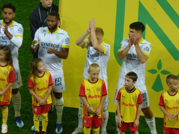 Gruppe junger Fußballspieler in Uniformen, die auf einem Ligue-1-Feld klatschen und einen Sieg feiern.