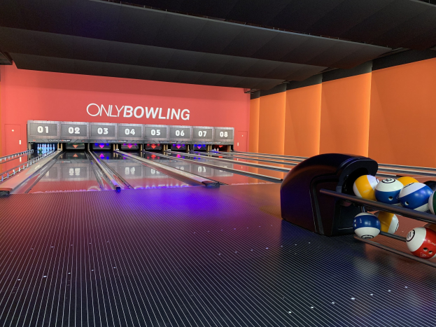 Eine Bowlingbahn mit Bowlingkugeln rechts, Pins in der Mitte und einer textbedeckten Wand im Hintergrund, mit der Decke darüber.